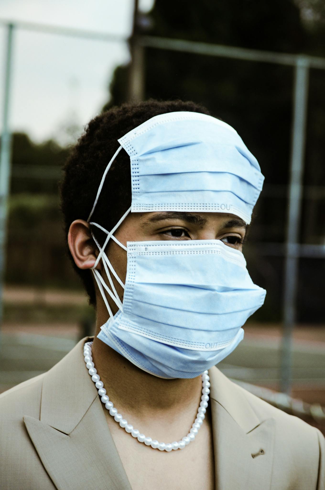 A creative portrait of a person wearing multiple masks outdoors, emphasizing unique fashion and health awareness.